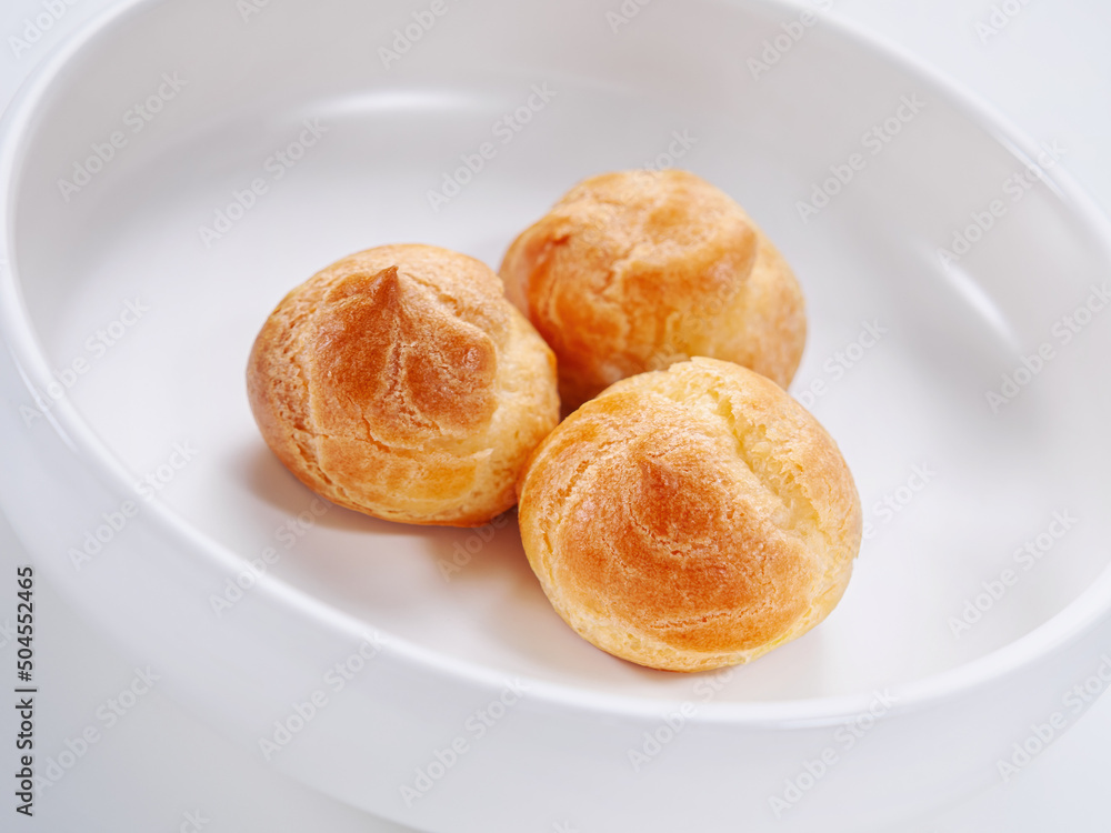 Bright fresh tasty profiteroles on a white plate. Close-up. Selective focus. Horizontal. High key. White background Bright fresh tasty profiteroles on a white plate. Close-up. Selective focus. Horizontal. High key. White background