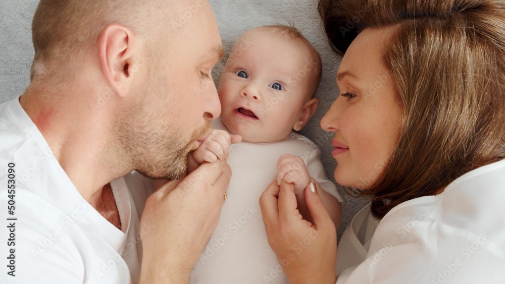 Happy family. Newborn baby with happy parents, top view. Healthy newborn baby in a white t-shirt with mom and dad. Close up Faces of the mother, father and infant baby. Cute Infant boy and parents