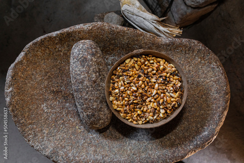 A jícara with grains / kernels of corn inside on a stone metate photo