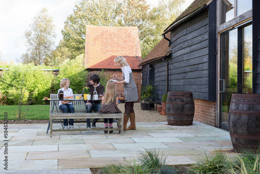 Family having breakfast outside on a bench. Converted barn housing. Family having breakfast outside on a bench. Converted barn housing.