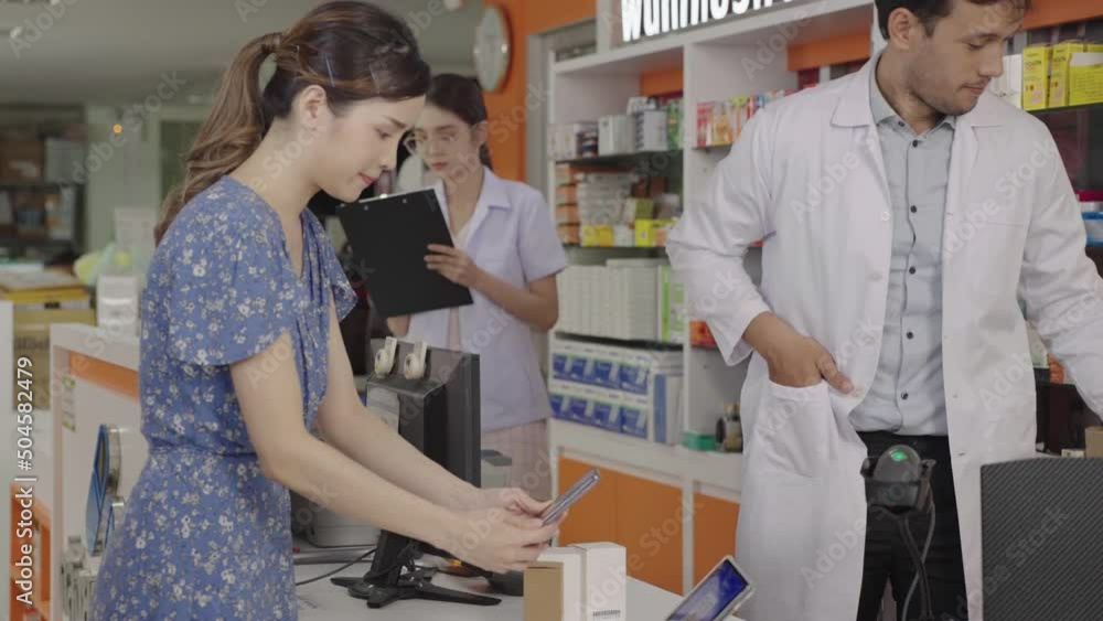 An Asian male pharmacist puts a pill box in a paper bag and a customer pays with an electronic wallet on her smartphone by scanning a QR code. An Asian male pharmacist puts a pill box in a paper bag and a customer pays with an electronic wallet on her smartphone by scanning a QR code.