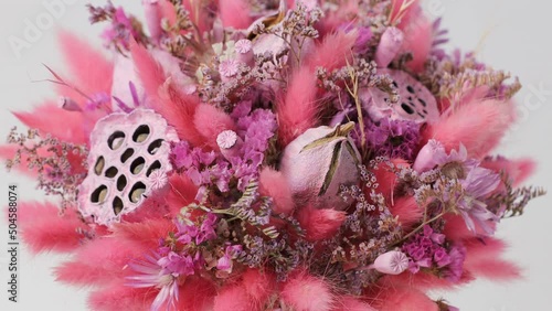 Pink bouquet of different beautiful dried flowers rotates around the axis on a white background