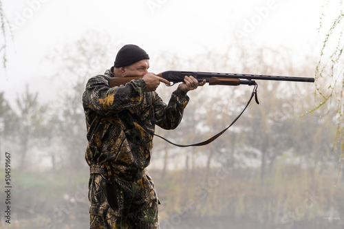 A male hunter with a rifle hunts and aims against the background of reeds and woods