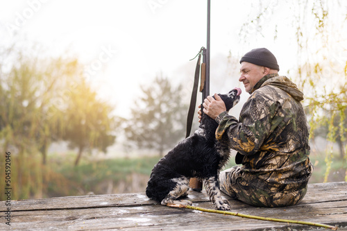 Fototapet Male hunter sits on a bridge against the backdrop of sunrise and forest with a l
