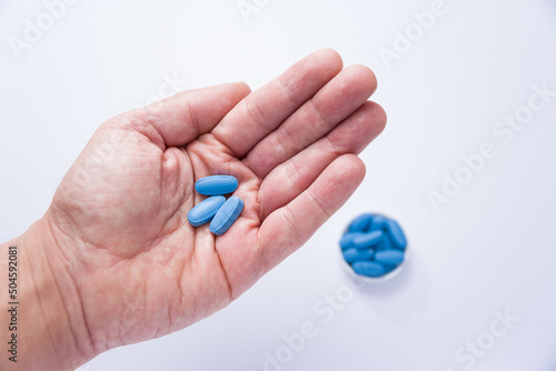 Male hand showing three pills in the palm and in the background a container full of blue tablets