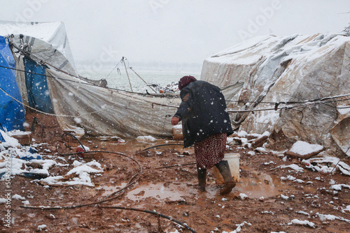 Fotografia A refugee woman walking in a snowy atmosphere, Syrian refugees in winter