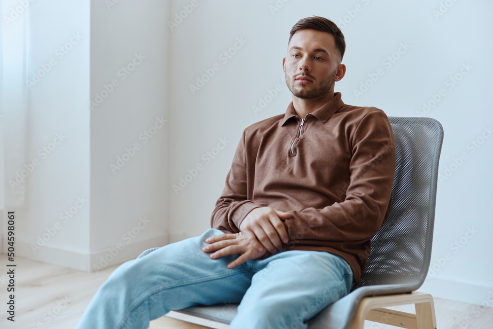 Frustrated sad young man guy leans on chair folded hands looks aside troubled with problems can not make decision have mental psychological trauma after bad break up sitting at home. Copy space