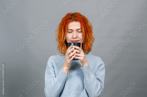Young red-haired woman with a drink with closed eyes from pleasure,