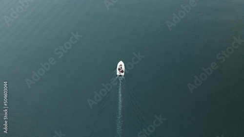 Small boat or yacht sailing alone on the estuary that leads to the sea on a cloudy day. Aerial top shot with drone following from the air.