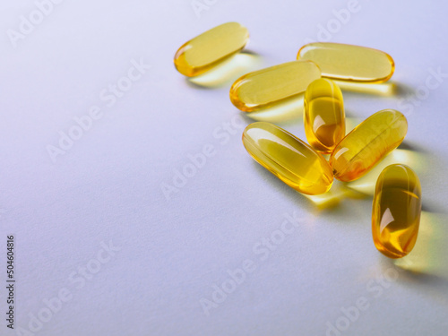 Yellow softgels lie on a violet surface. Fish oil. Vitamins and a healthy lifestyle. Background or backdrop. Copyspace on the left. Softgel close-up. Omega-3 fatty acids. Macro