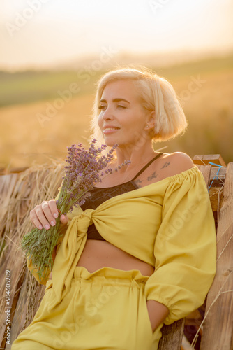 Pretty young woman in yellow among rural field with golden oat field on sunset background