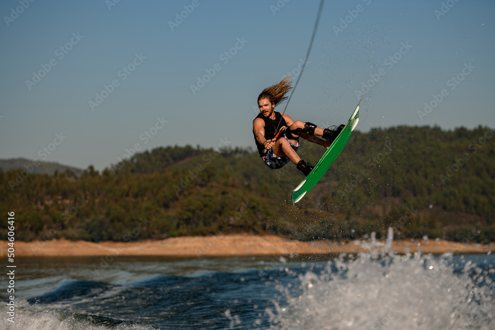 handsome healthy active man masterfully jumping over splashing wave on wakeboard