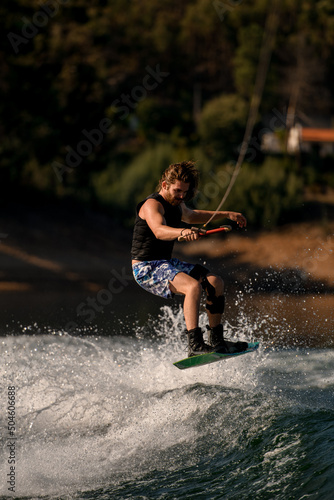 Fototapeta Naklejka Na Ścianę i Meble -  Athletic guy holds rope and jumps at the wave on wakeboard.