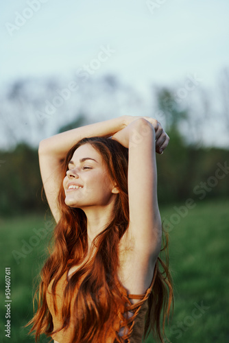 A woman warms up and stretches her arms up in nature in a green park after an outdoor sports workout in the sunset sunlight. The concept of a healthy lifestyle and an athletic body