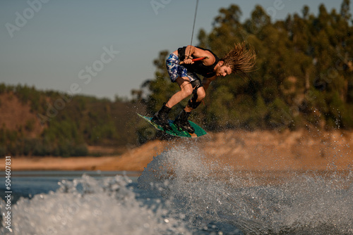 great photo shot of man masterfully jumping over splashing wave on wakeboard photo