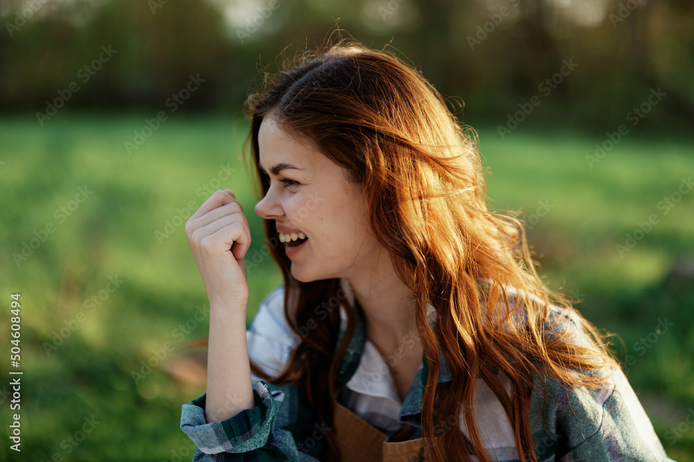 Close-up portrait of the face of a smiling, beautiful redheaded young woman in nature in a green park at sunset