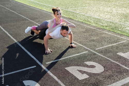 Loving couple trains together at the stadium, a man does push-UPS and a girl lies on his back
