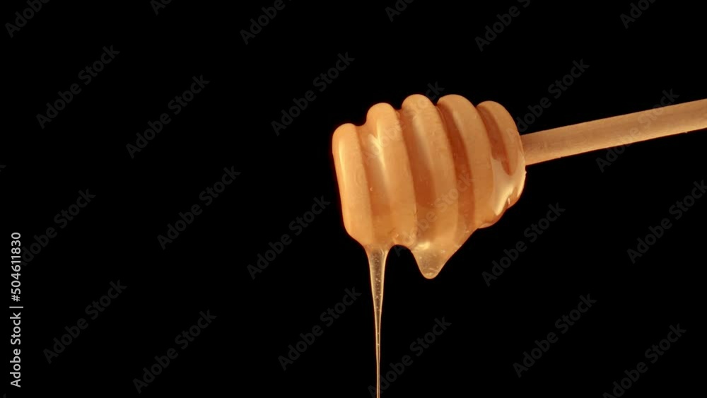 Honey dripping, pouring from a honey dipper on a black isolated background. Healthy organic thick honey dipping from a wooden honey spoon, close up. Golden liquid, sweet molasses, sugar syrup. Honey dripping, pouring from a honey dipper on a black isolated background. Healthy organic thick honey dipping from a wooden honey spoon, close up. Golden liquid, sweet molasses, sugar syrup.