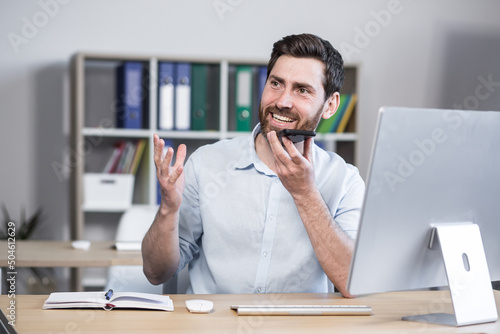 Fotografija Cheerful and happy man records audio messages, freelance businessman in office,