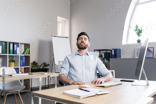 Businessman in the office with closed eyes performs breathing exercises, freelancer working on the computer