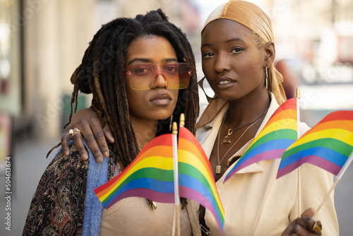 LGBTQ same sex black women couple waving rainbow flags on a city street photo