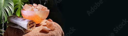 Banner of himalayan salt lamps and towel rotating on table in dark room. Boost mood, improve sleep, ease allergies, reduce anxiety and clean the air. Copy space