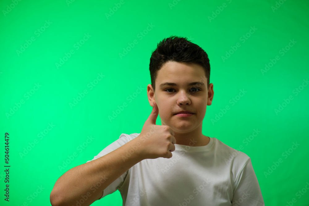 a 12-14-year-old boy on a green background looks at the camera and shows his finger a 12-14-year-old boy on a green background looks at the camera and shows his finger