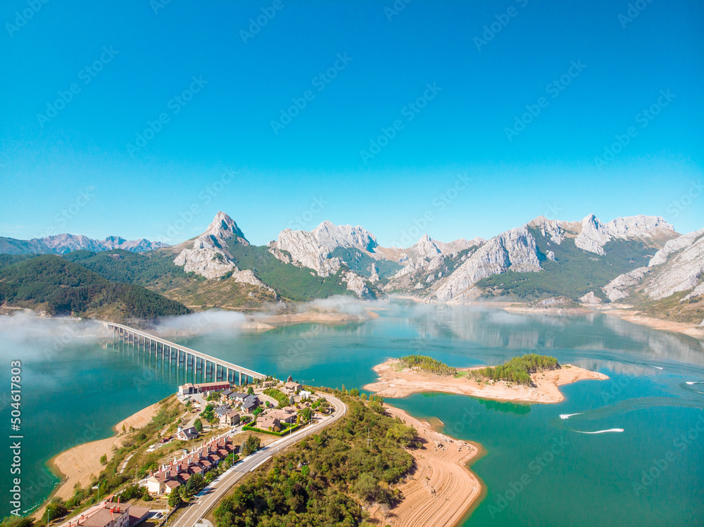 aerial drone shot of a swamp located in the town of Riaño, a village with a road with a bridge that divides the lake on a sunny day with the stone mountains in the background