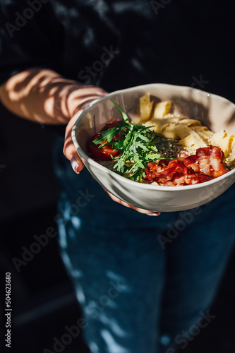 bacon, arugula, tomato, breakfast cereal, the dish is held by a waiter in his hand