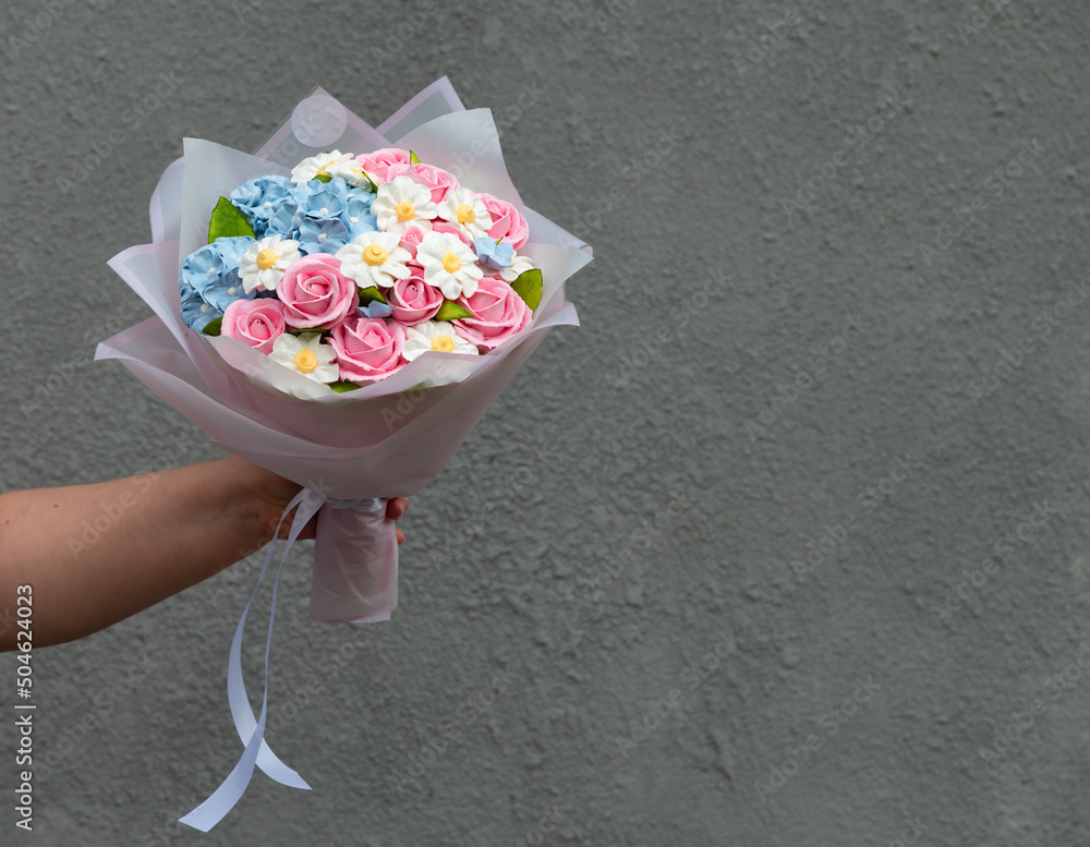 Bouquet of marshmallows. Rose, hydrangea and chamomile in a festive package with a white ribbon. Female hand holds flowers. Against the background of a gray wall with a rough texture Bouquet of marshmallows. Rose, hydrangea and chamomile in a festive package with a white ribbon. Female hand holds flowers. Against the background of a gray wall with a rough texture