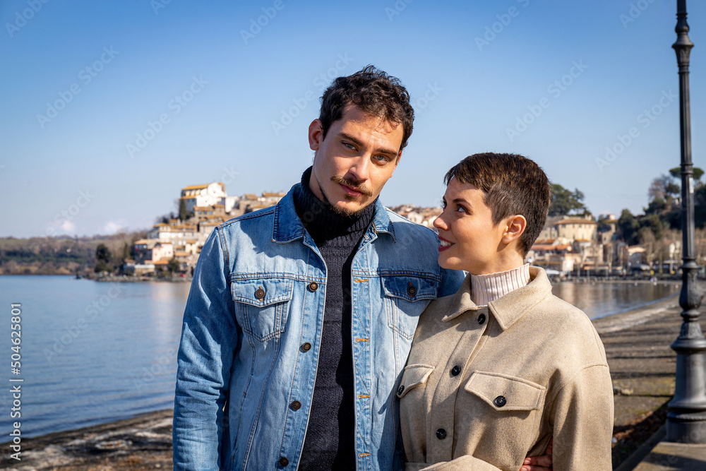 Young couple walks on the shore of Lake Bracciano. Beautiful couple traveling to Anguillara Sabazia in Lazio, Italy. Romantic atmosphere and copy space for your message.