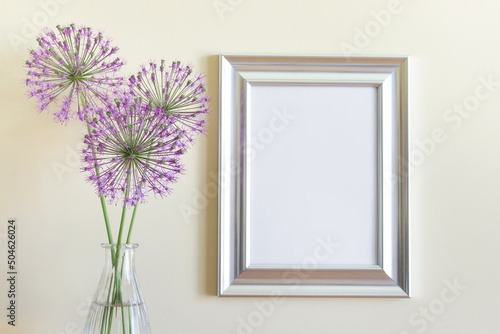 Mockup template with blank silver frame and purple summer garlic flowers next to yellow wall.