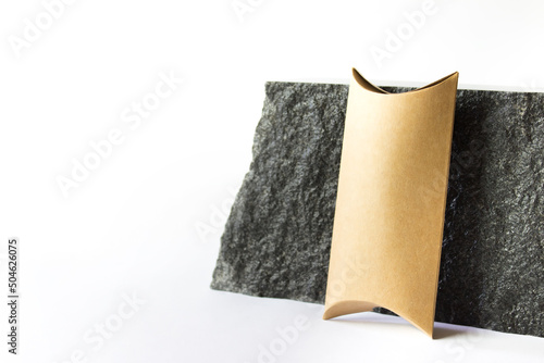 Mockup template with craft paper guft box standing next to raw natural black stone on white background. Image with copy blank space. photo