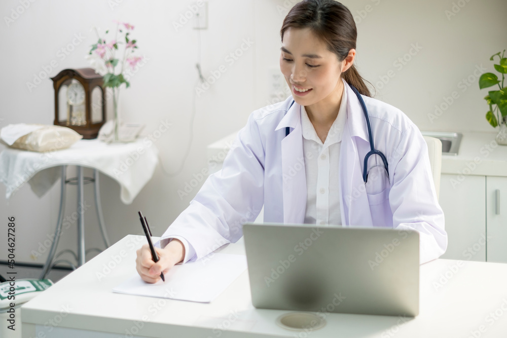 Young Female Doctor in white coat sitting at her workplace working. Doctor sitting at desk and writing a prescription for her patient. Smiling female doctor working in doctor’s office. Young Female Doctor in white coat sitting at her workplace working. Doctor sitting at desk and writing a prescription for her patient. Smiling female doctor working in doctor’s office.