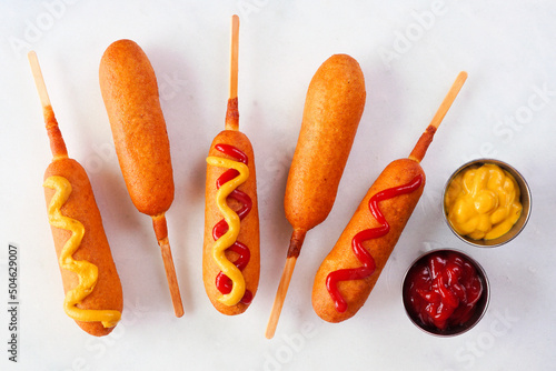 Corn dogs with a variety of toppings. Above view over a white marble background.