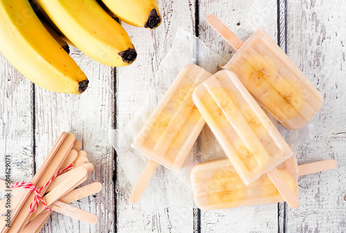 Healthy banana yogurt popsicles in a cluster. Top view table scene on rustic white wood background