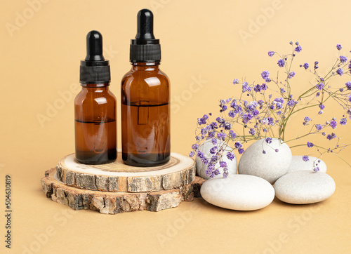 A wooden podium, stones, a sprig of gypsophila and two bottles with an eyedropper filled with oil or essence. Body care concept, natural spa cosmetics