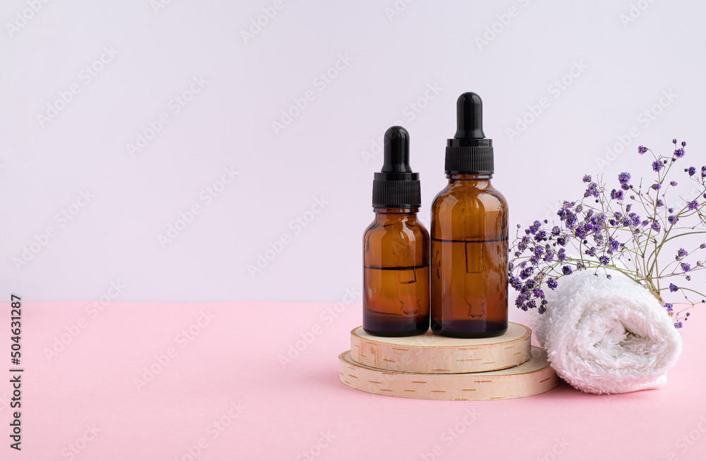 A wooden podium, a white napkin, two bottles with a pipette filled with hyaluronic acid, oil or essence. Body care concept, natural spa cosmetics