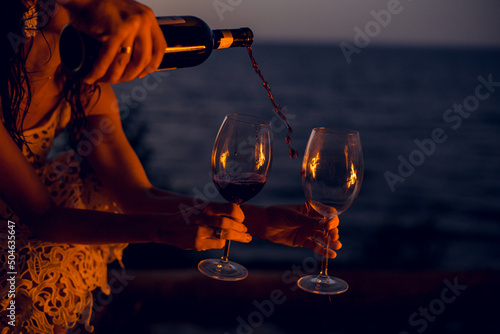 the process of filling a glass with red wine on the beach at sunset by the fire