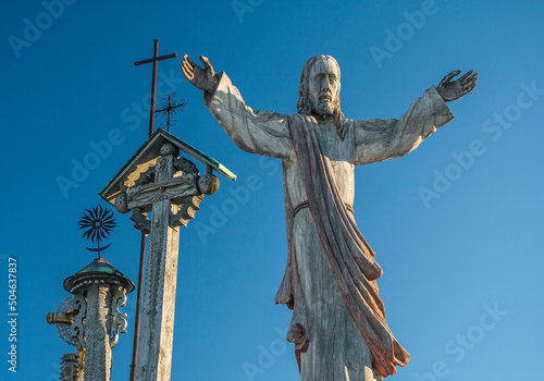 Lithuania - Siauliai - The wooden sculpture of Christ along with some crosses behind at the entrance onto Hill of the Crosses (kryziu kalnas), the famous lithuanian religious landmark photo