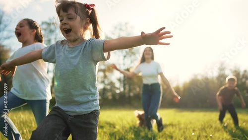 Children play in spring vacation park.Active happy group of kid run with a dog on grass in field in summer.Family in nature with pet.Child on play.Happy family concept.School in garden with dog