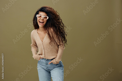 FASHION CONCEPT. Enjoyed pretty tanned curly Latin female in casual things sunglasses hold hand on jeans posing isolated over pastel olive green background. Copy space Mockup Banner. Fashion offer