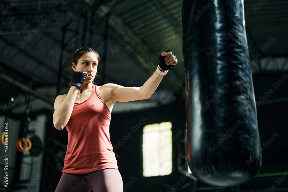 Determined athletic woman hitting punching bag during sports training in gym.