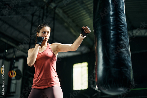 Determined athletic woman hitting punching bag during sports training in gym.