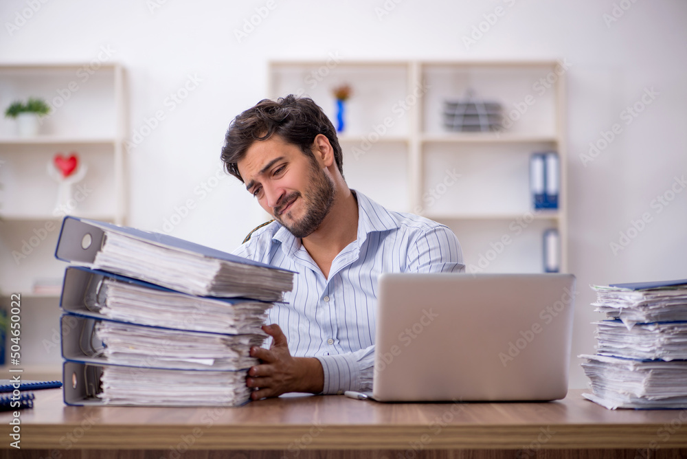 Young male employee unhappy with excessive work in the office Young male employee unhappy with excessive work in the office