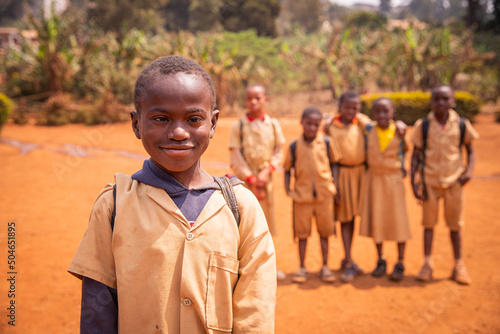 African schoolboy with Down syndrome in the schoolyard with his school mates out of focus in the background.