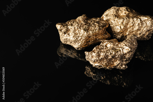 Gold nuggets on black reflective surface, space for text