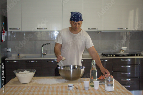 Photo Man in the home kitchen putting yeast in a bowl where he prepares dough for bre