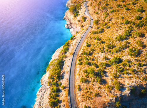 Fototapeta Naklejka Na Ścianę i Meble -  Aerial view of mountain road near blue sea with sandy beach at sunset in summer. Oludeniz, Turkey. Top view of road, trees, azure water, mountain. Beautiful landscape with highway, rocks, sea coast