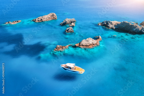 Aerial view of speed boat on blue sea at sunset in summer. Motorboat on sea bay, rocks in clear turquoise water. Tropical landscape with yacht, stones. Top view from drone. Travel in Oludeniz, Turkey © den-belitsky